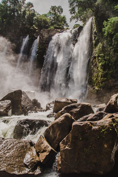 Free Scenic view of powerful waterfalls cascading over boulders in a lush forest setting. Stock Photo