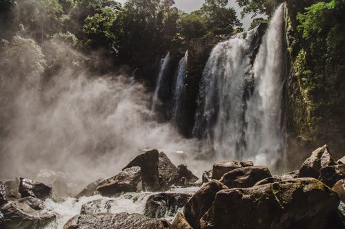 Free A breathtaking view of cascading waterfalls surrounded by lush forest and rocky terrain. Stock Photo