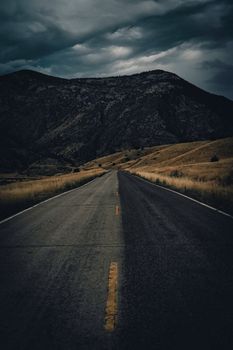 A solitary road leads into dark mountains under an ominous cloudy sky.