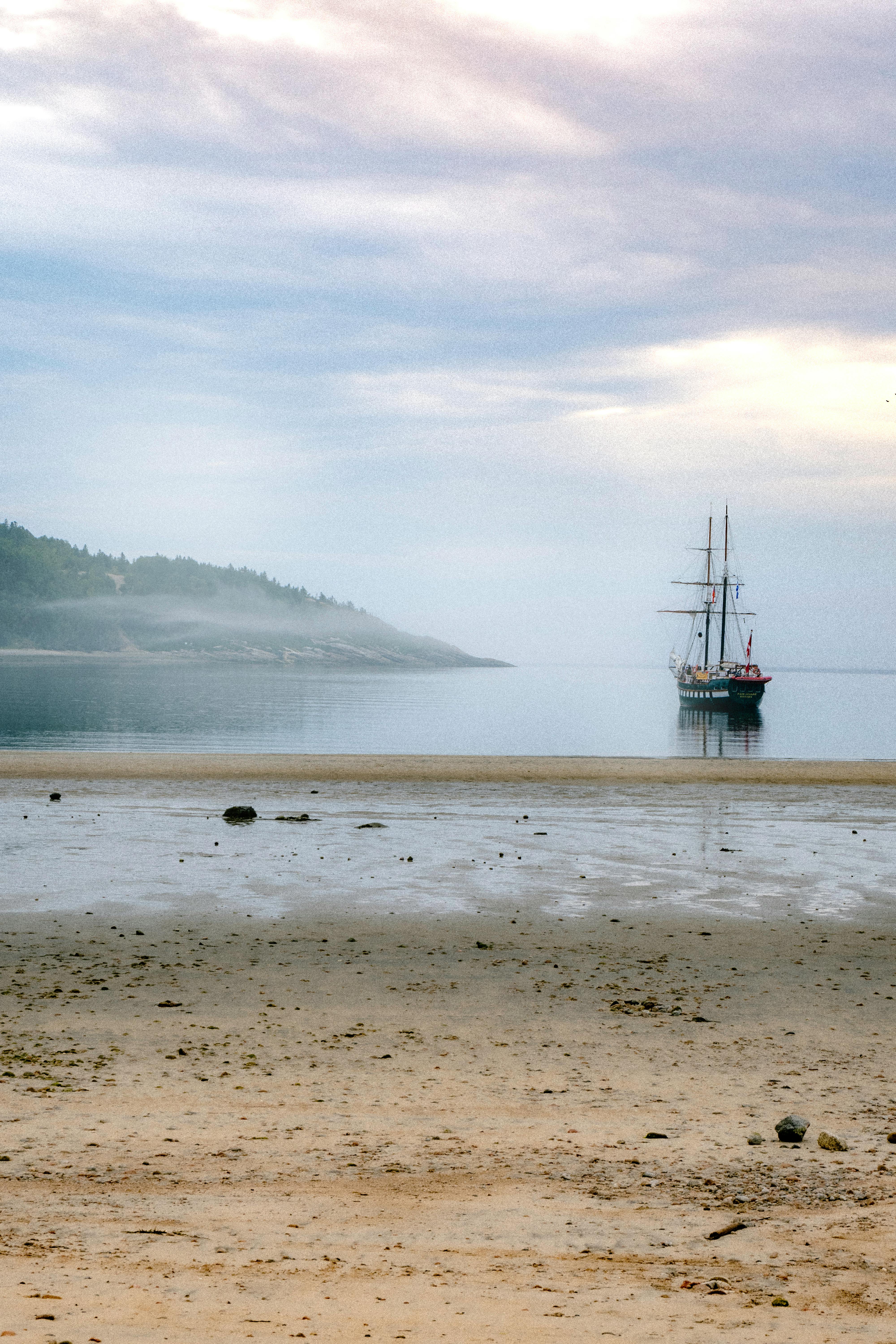 Tranquil seascape featuring a solitary sailboat near an empty beach at dawn.
