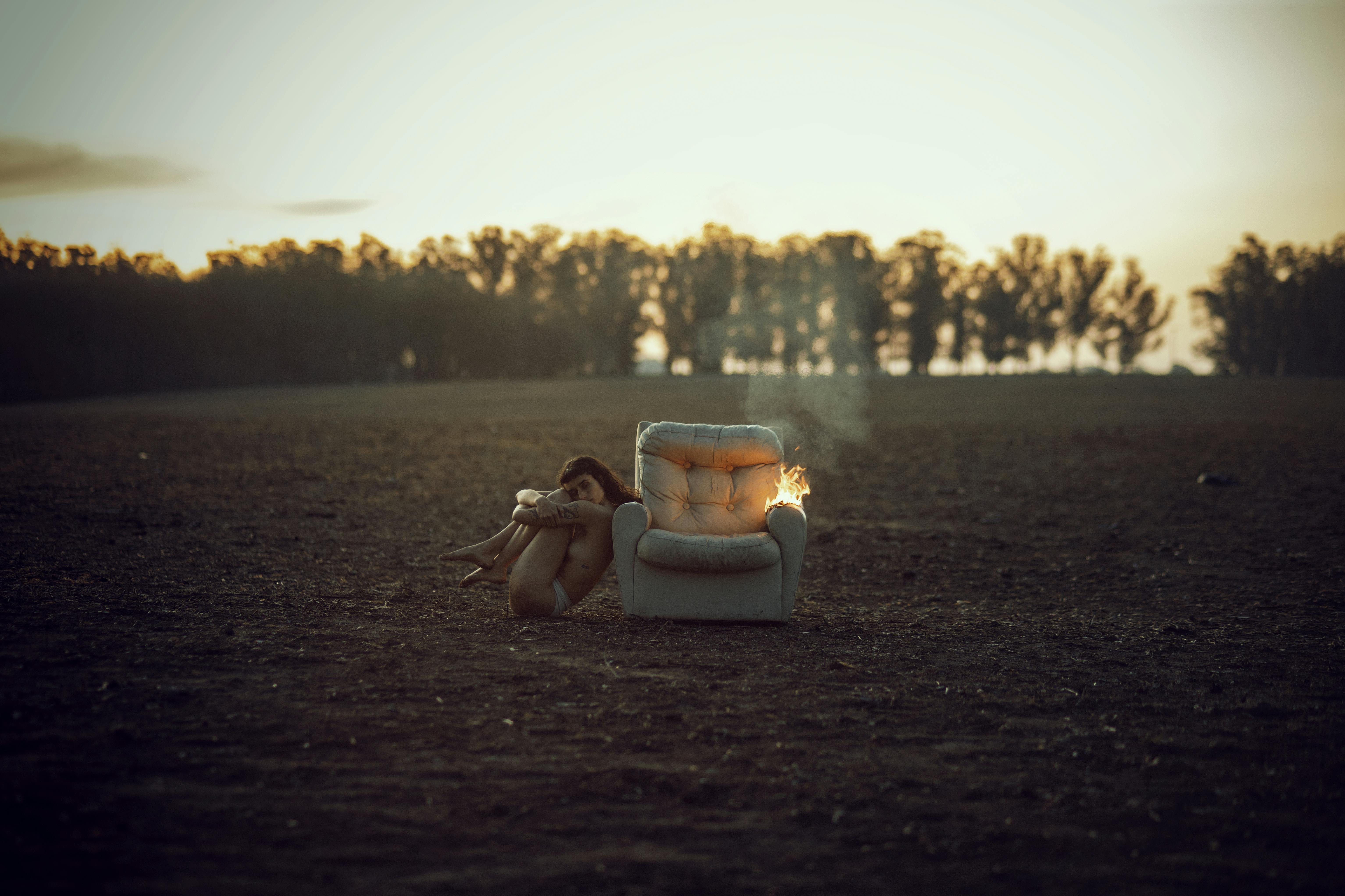 naked woman sitting near burning chair in field