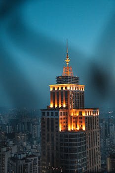 A brightly lit skyscraper stands tall in the urban skyline during twilight, showcasing its modern architecture.