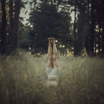 A woman performs a headstand in tranquil forest surroundings, capturing the essence of outdoor yoga and mindfulness.