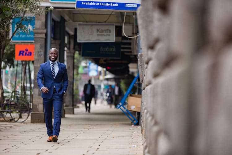 A Man In Blue Suit Walking On Sidewalk