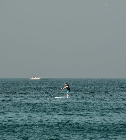 Free A person paddleboarding on the vibrant sea with a boat in the background, set in Dubai. Stock Photo