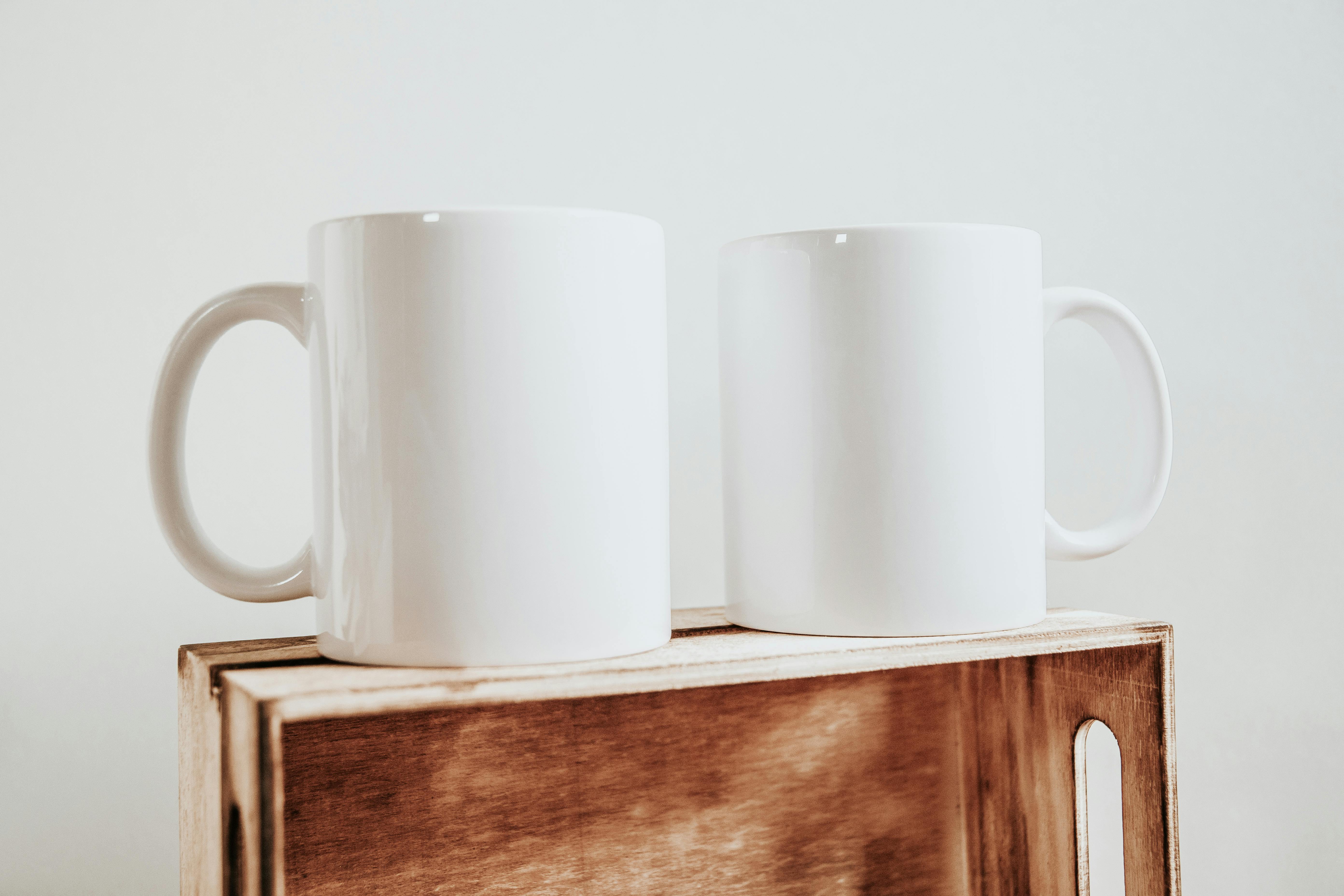 Two minimalist white ceramic mugs on a wooden box, perfect for coffee or tea.