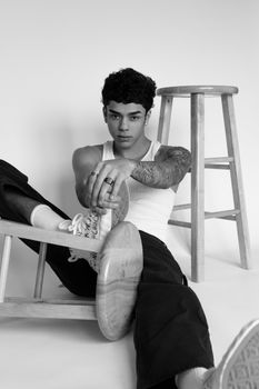 Black and white studio photo of a young model posing with tattoos and stool.