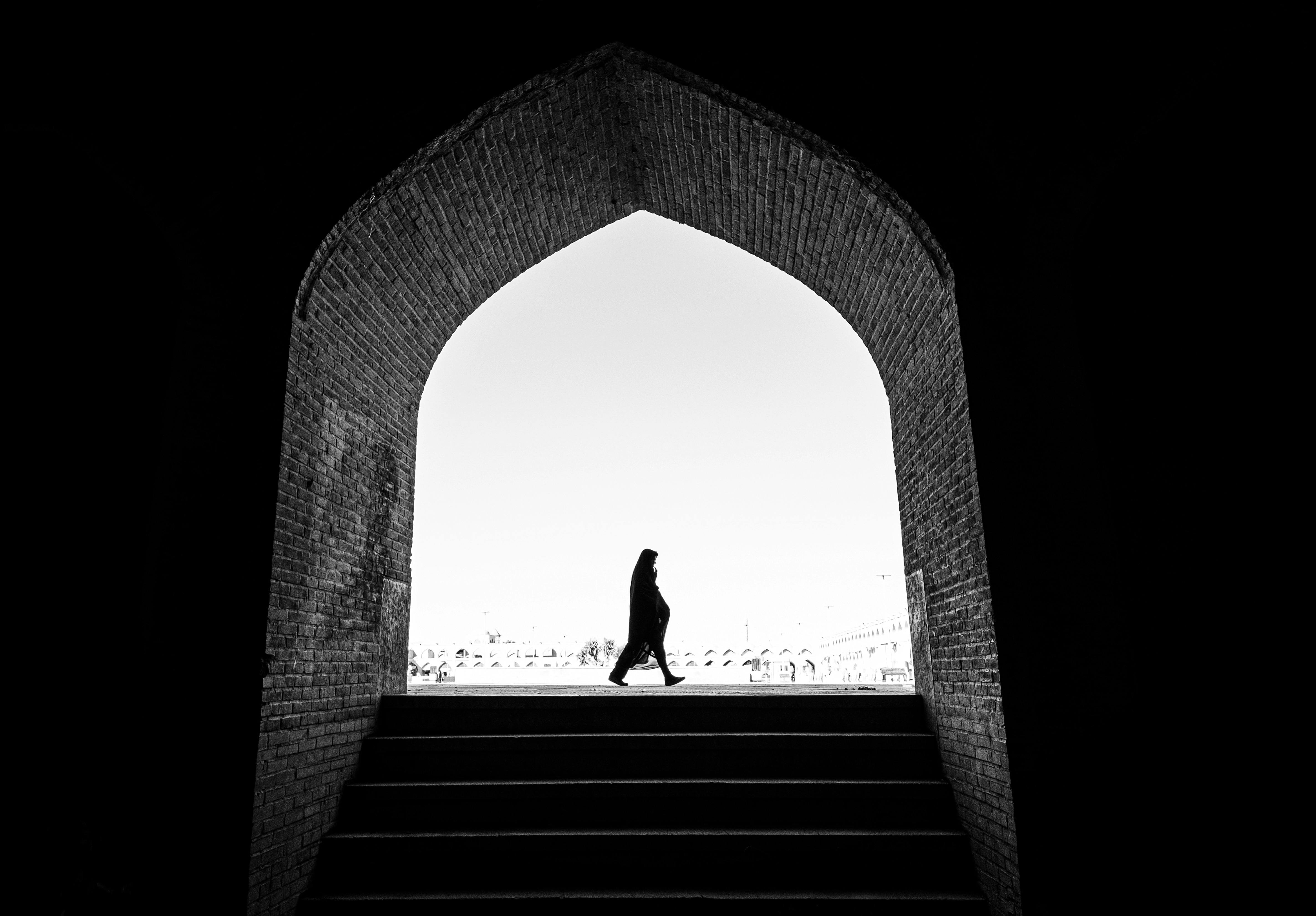 A woman in silhouette walks under an archway in Isfahan, Iran, showcasing stunning architecture.