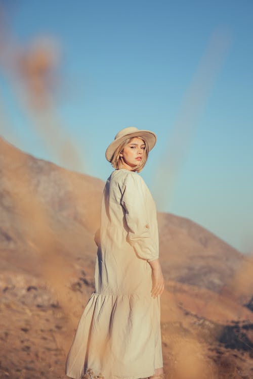 Woman in a Dress and Hat Standing near Mountains