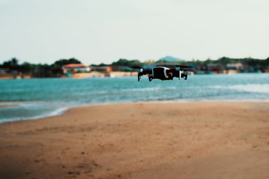 A drone hovering over a serene beach with ocean waves in the background.