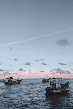 Fishing boats float peacefully on the ocean beneath a pastel sky at twilight, showcasing serene seascape beauty.
