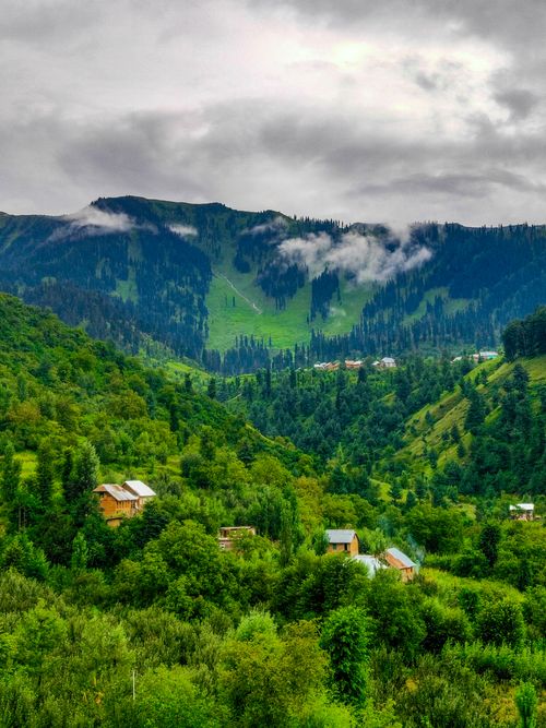 Free Scenic landscape of a verdant valley surrounded by mountains under a cloudy sky. Stock Photo