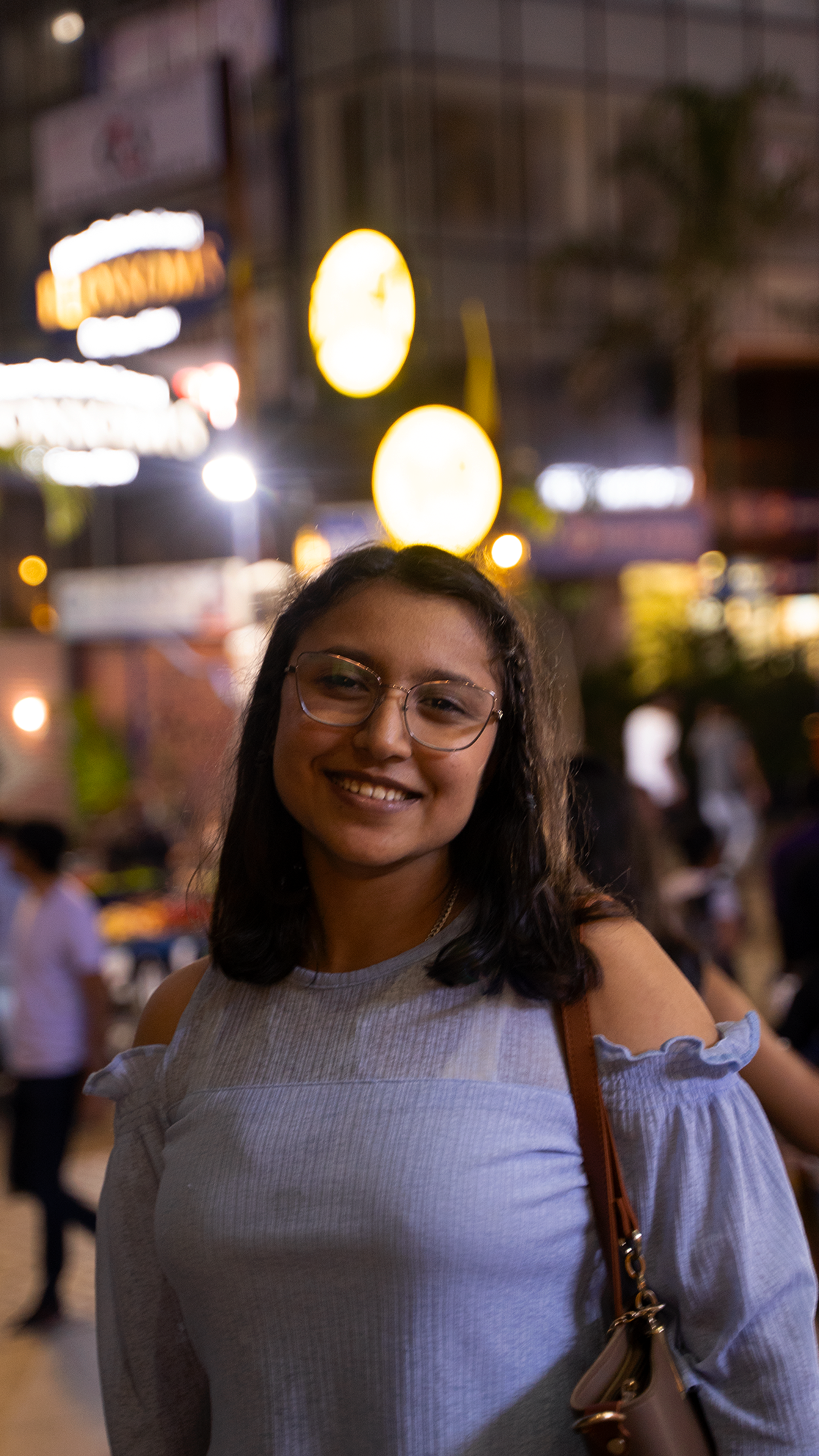 Happy woman with glasses smiling at night in city street, vibrant lights in background.