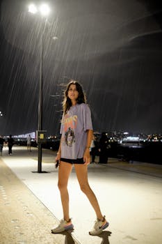 A man confidently poses on a well-lit street during a rainy night, showcasing urban fashion.