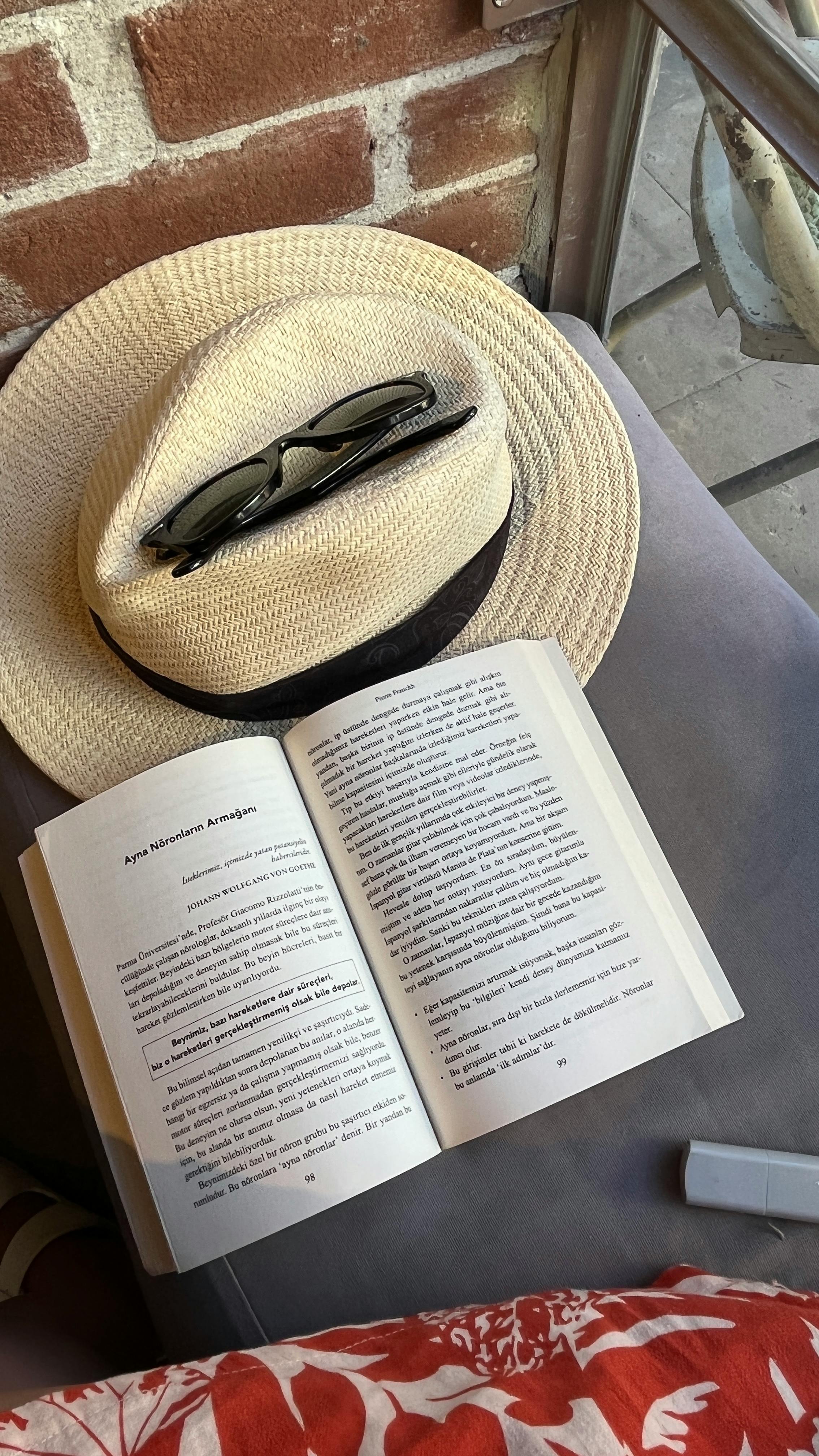 Open book with sunhat and sunglasses on a chair, perfect for summer reading outdoors.