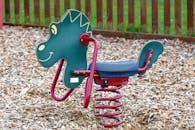 在铺有木片的户外操场上，一位色彩缤纷的恐龙主题骑手正进行春季骑行