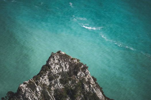 High-angle view of a rocky cliff meeting vibrant turquoise waters, showcasing natural beauty.