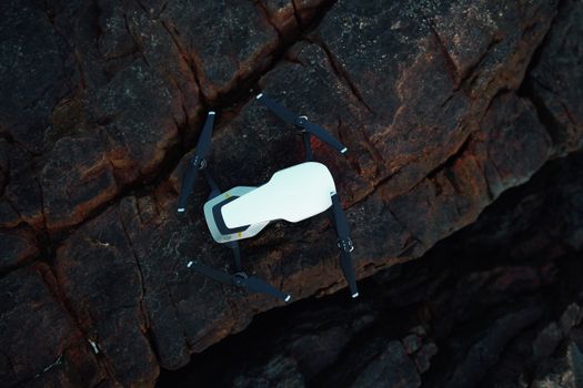 Top view of a white drone resting on textured dark rocks. Perfect for tech themes.