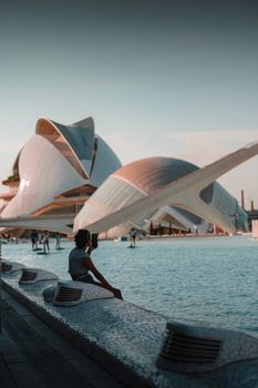 A person relaxes by the water with iconic modern architecture in the backdrop.