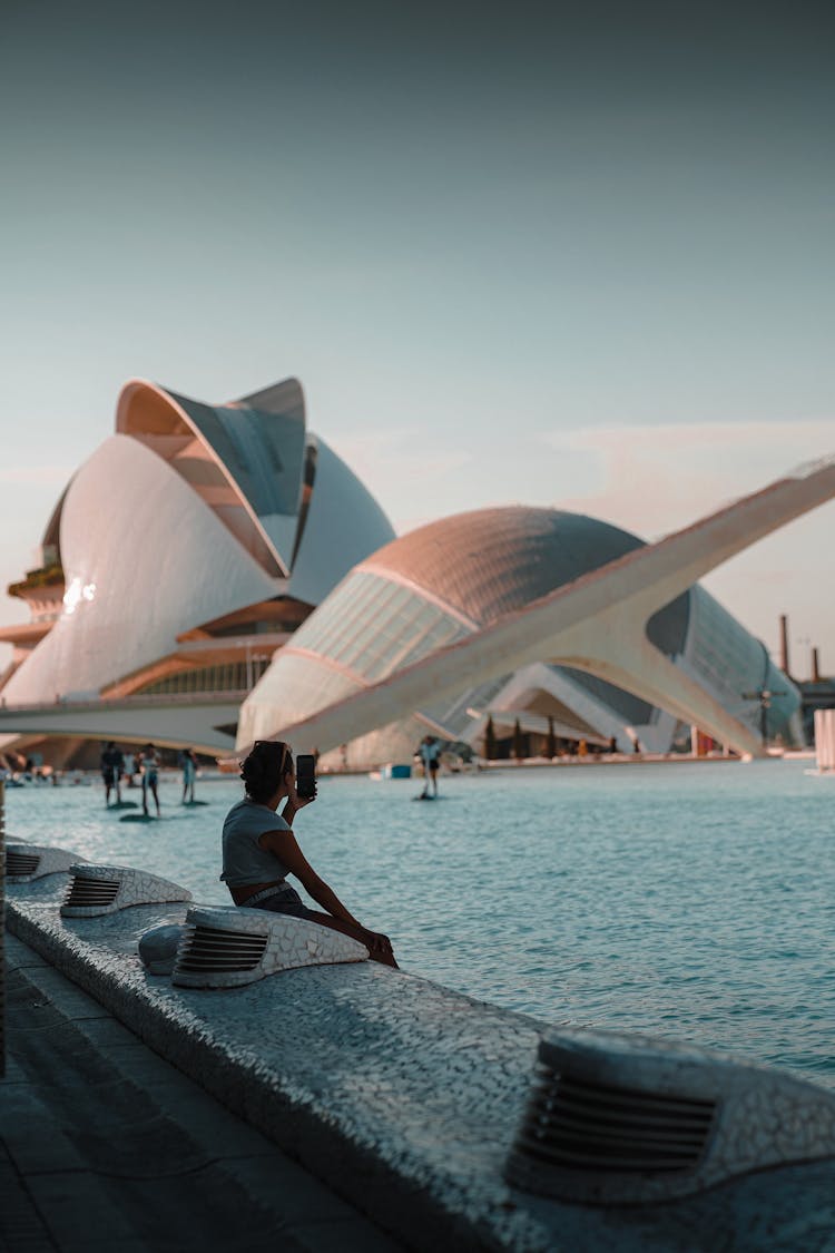 Person Sitting Near Pool Near Futuristic Buildings