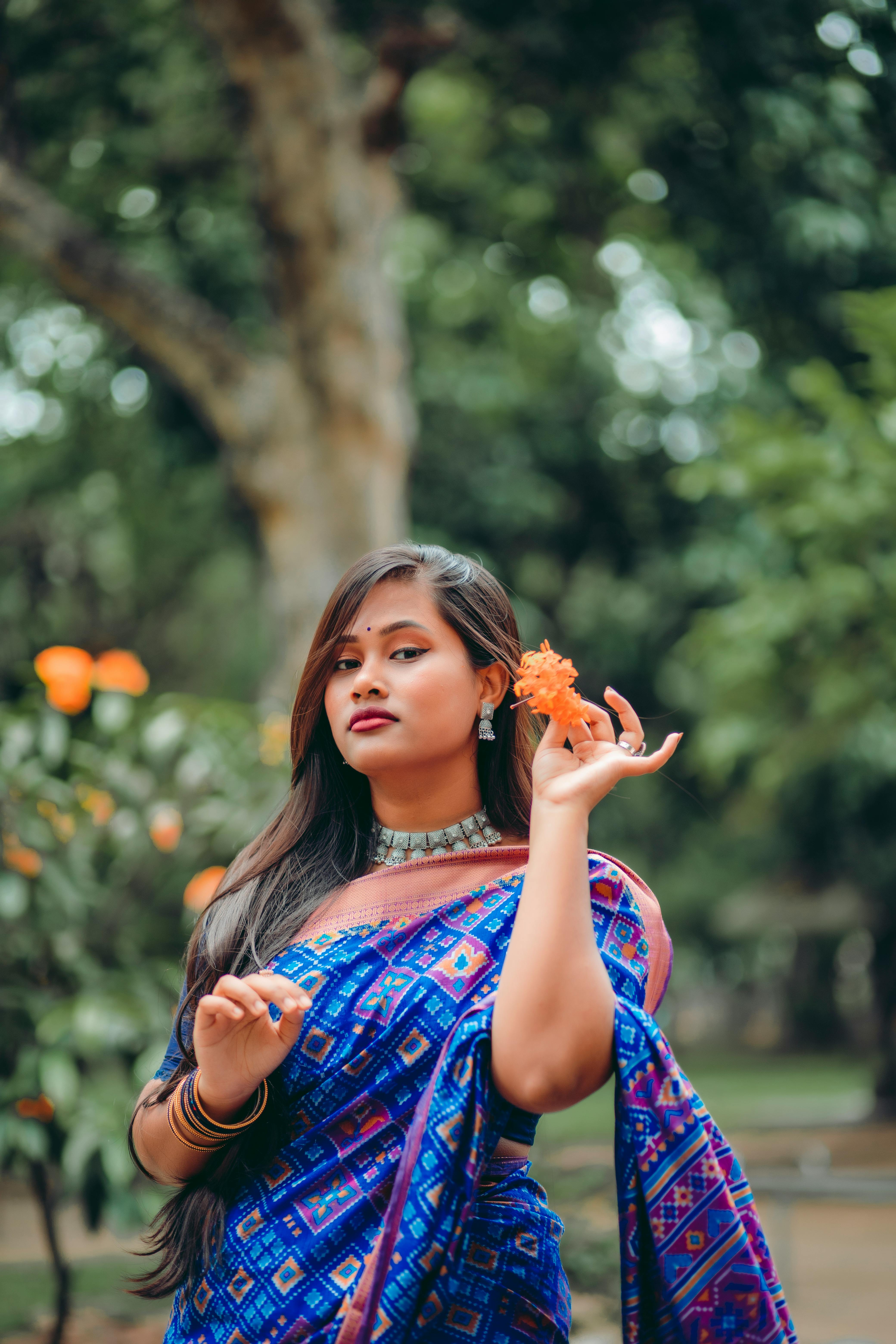 South Asian woman in traditional sari holding an orange flower outdoors in Dhaka, Bangladesh.