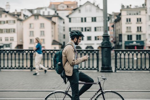 A man on a bicycle uses his smartphone while paused on a city bridge during the day.