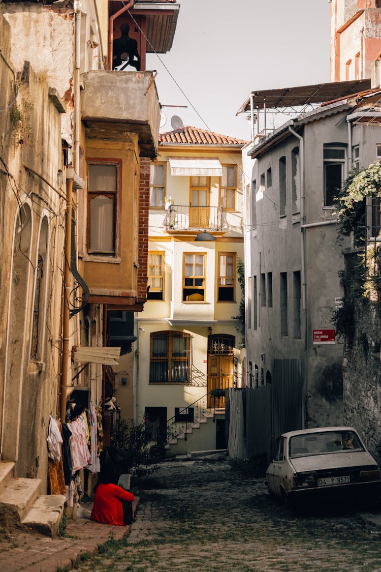 Person Sitting On Sidewalk Of Narrow Paved Alley