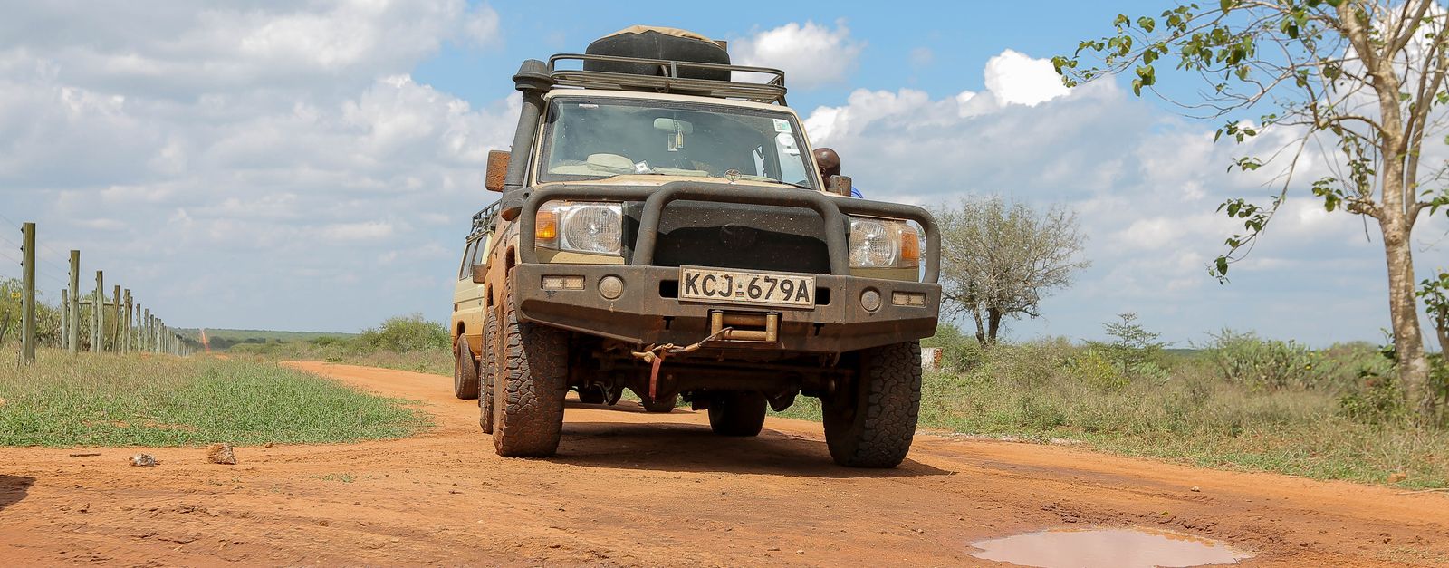 A rugged 4x4 SUV navigating a muddy outdoor trail under a bright sky.