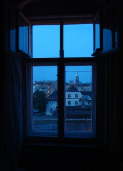 Urban view through a window at dusk, showcasing buildings in blue twilight.