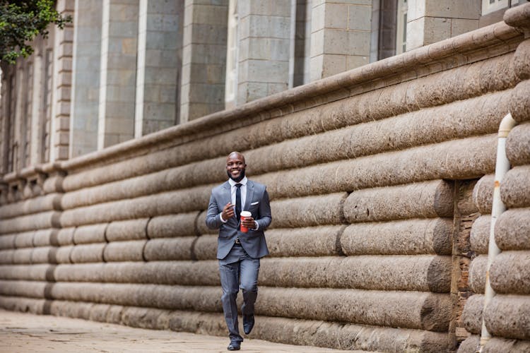 Smiling Man In A Suit Running With A Coffee Cup