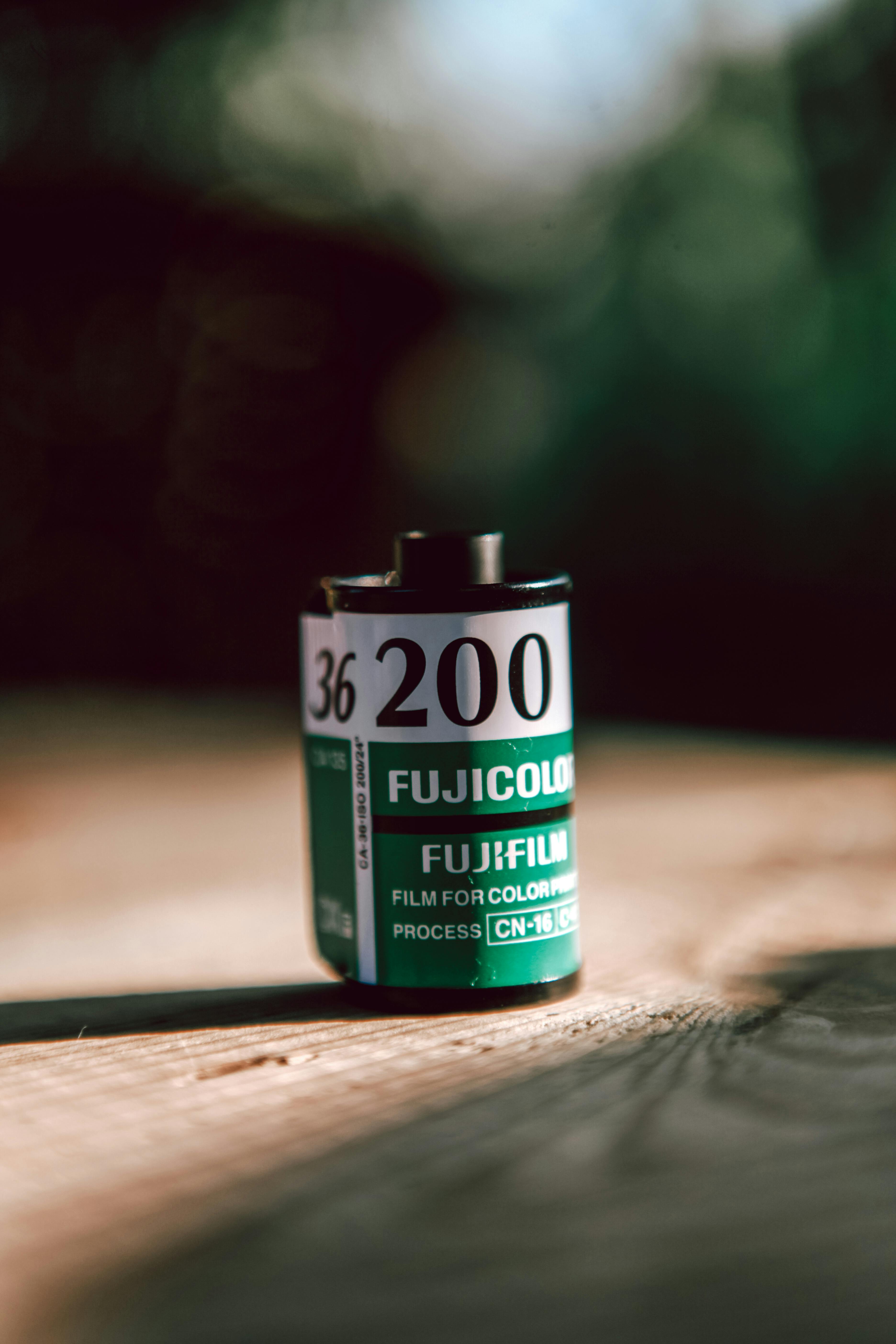 A Fujicolor 200 film roll sits on a wooden table, highlighting vintage photography.