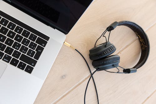 Headphone Berkabel Hitam Ditancapkan Di Macbook Pro Pada Permukaan Kayu Coklat