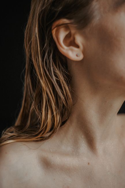 Artistic close-up portrait of a woman with wet hair and visible collarbone in a studio setting.
