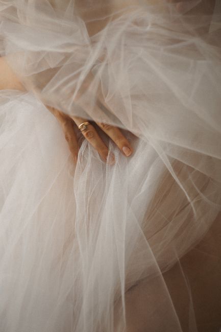 A close-up image of a delicate hand adorned with a ring, gracefully touching elegant tulle fabric.