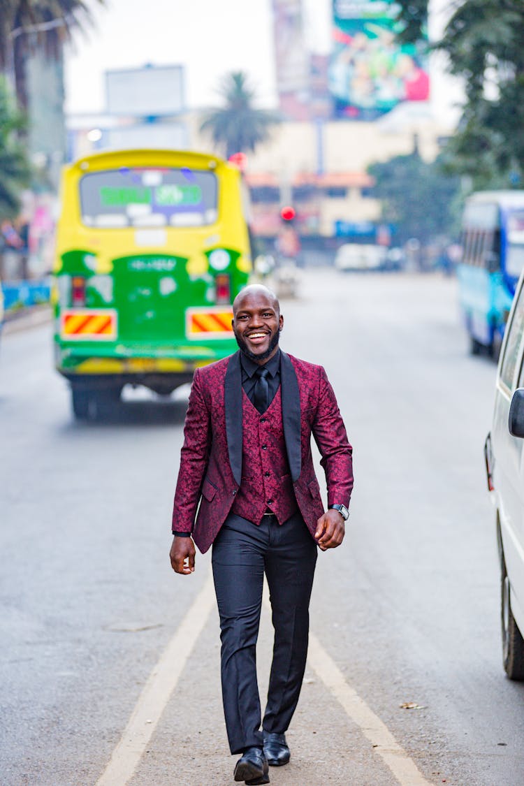 A Bald Man Wearing Maroon Suit Walking On The Road 