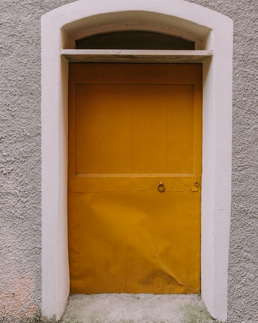 Close-up of a rustic yellow door set in a textured wall, featuring an arched frame.