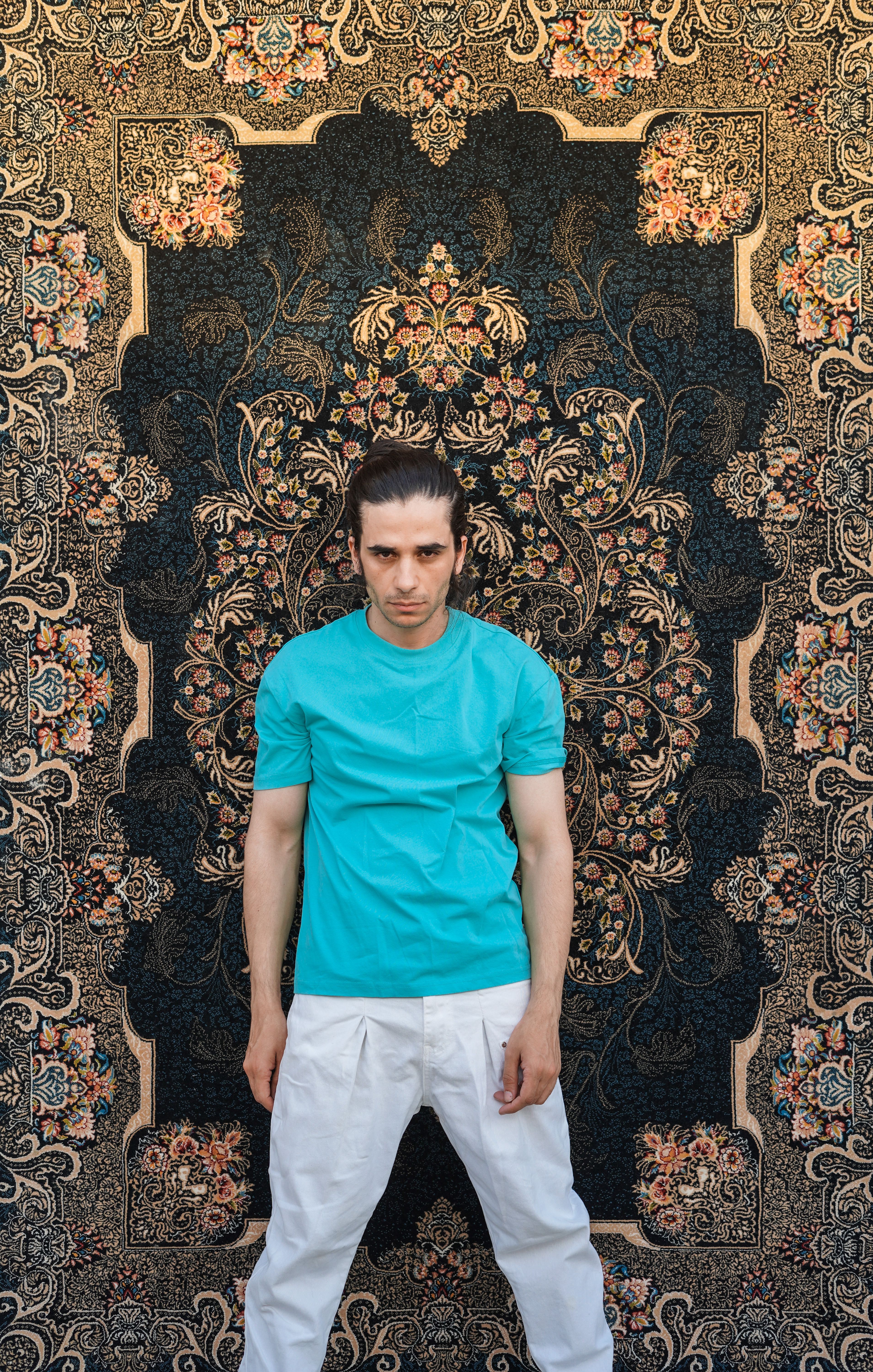 Young man stands on intricate Persian rug, highlighting traditional design.