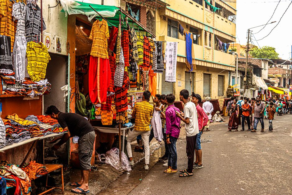 A bustling street market scene with colorful textiles and shoppers on an urban street in India.
