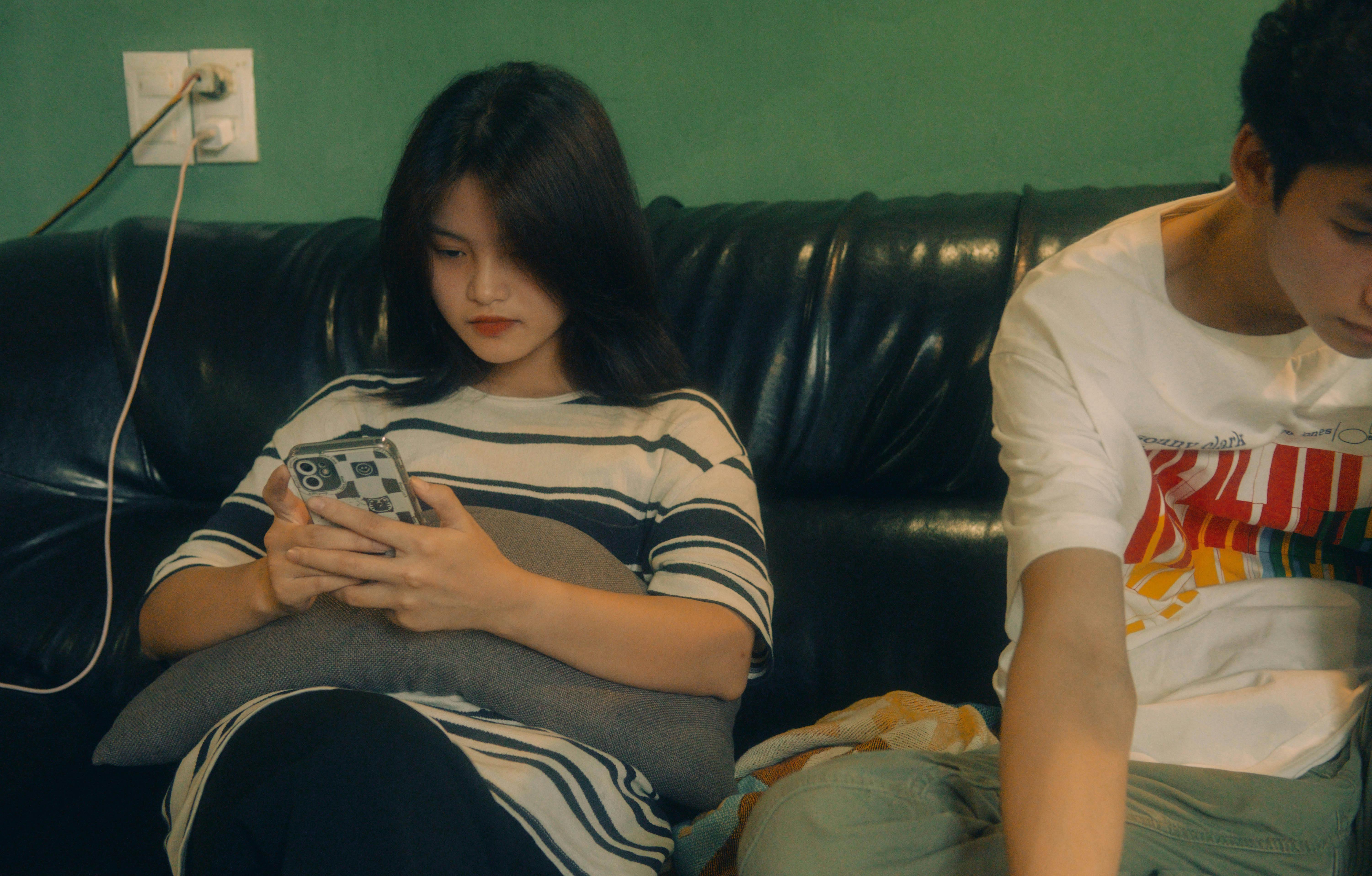 Two teenagers sitting on a sofa, focused on their smartphones indoors.