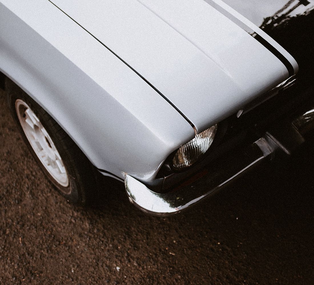 The front of a classic white car with racing stripes