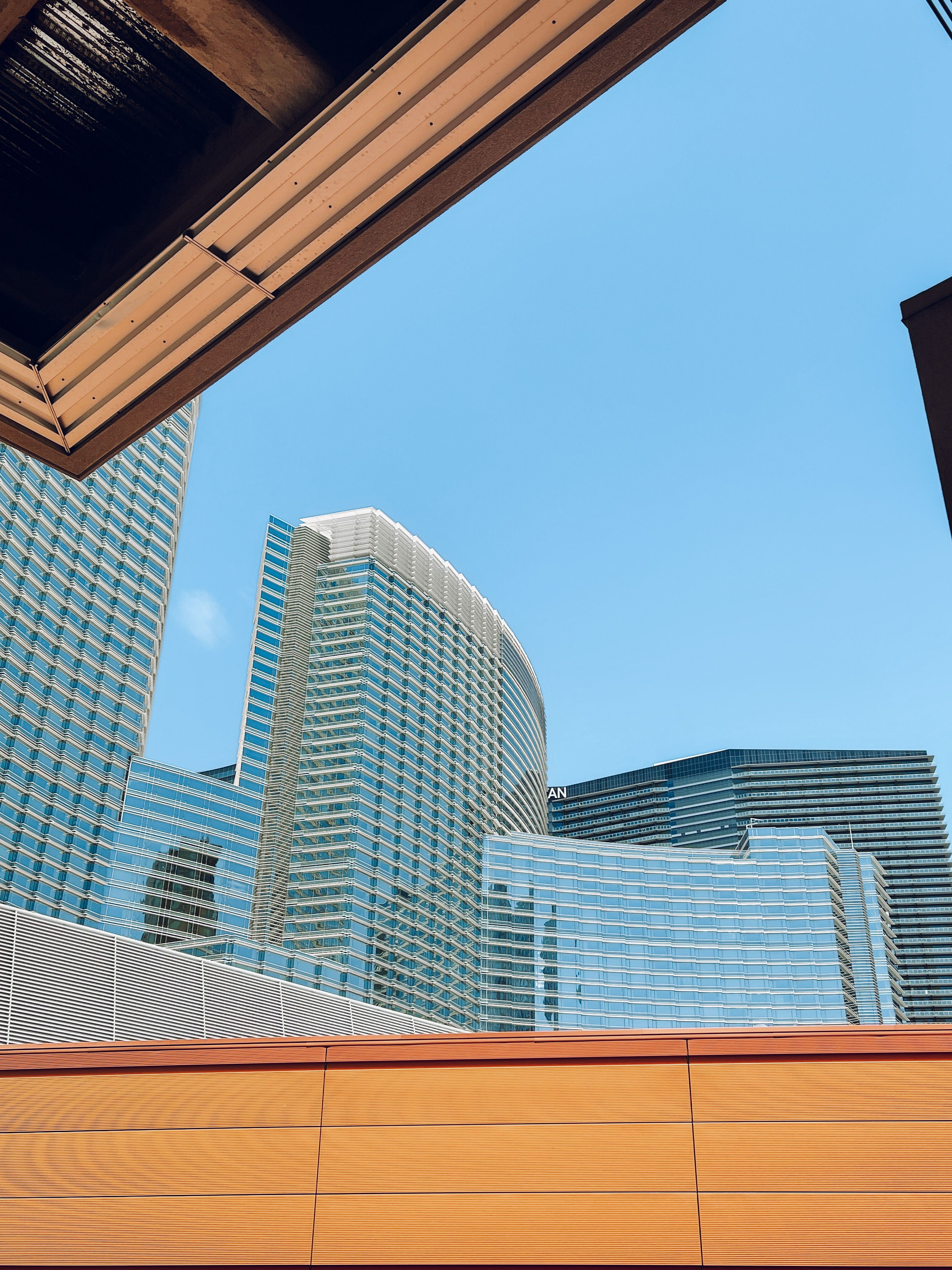Upward view of sleek skyscrapers framed by architectural elements under a clear blue sky.