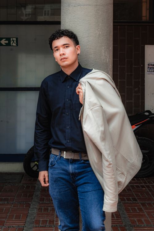 Free A young man poses confidently with a jacket slung over his shoulder in an urban environment. Stock Photo
