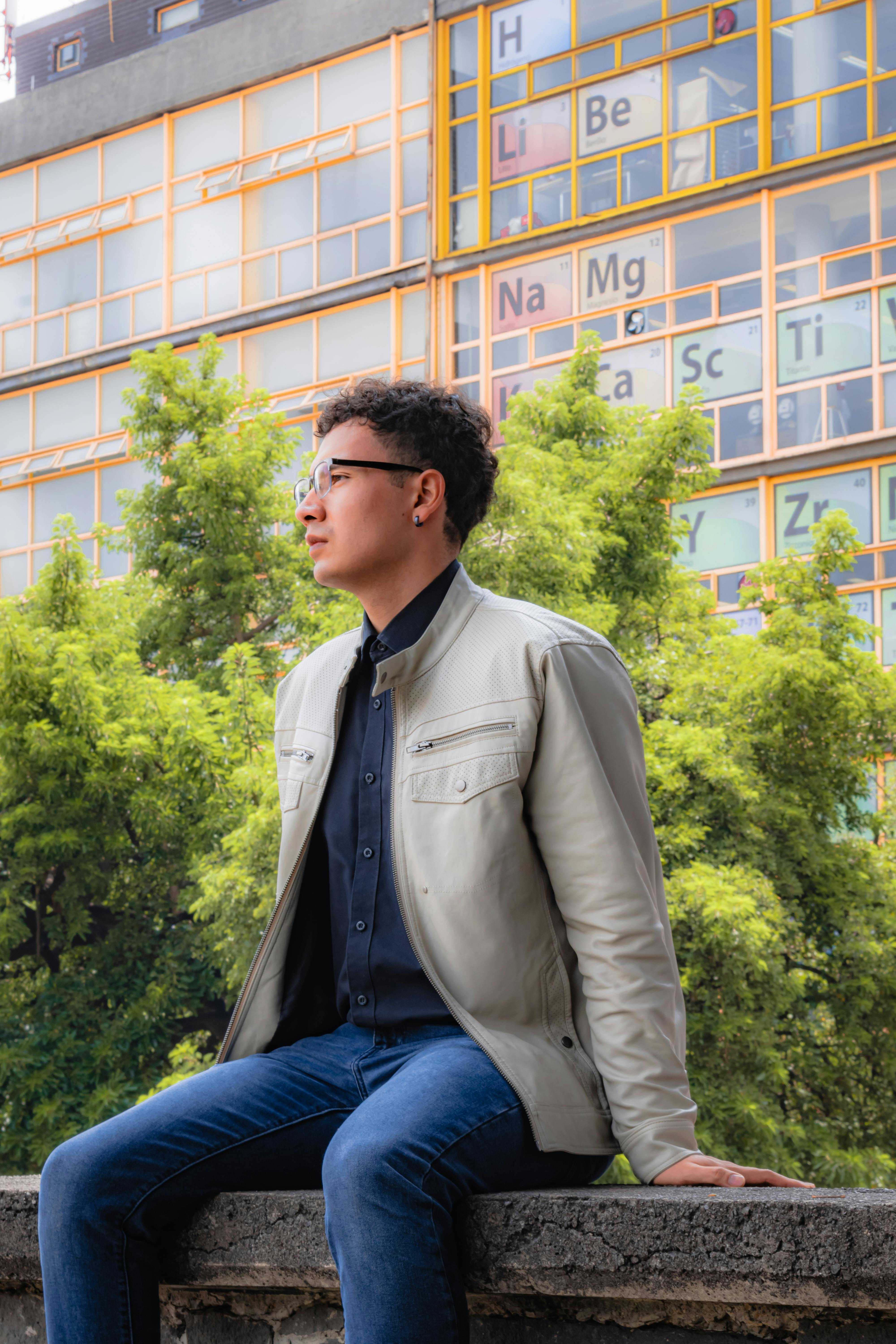 Stylish man in glasses sits against a modern architectural backdrop.