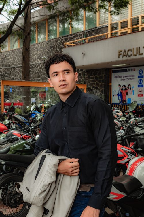 Free Young man in black shirt poses outdoors with parked motorbikes, looking serious. Stock Photo