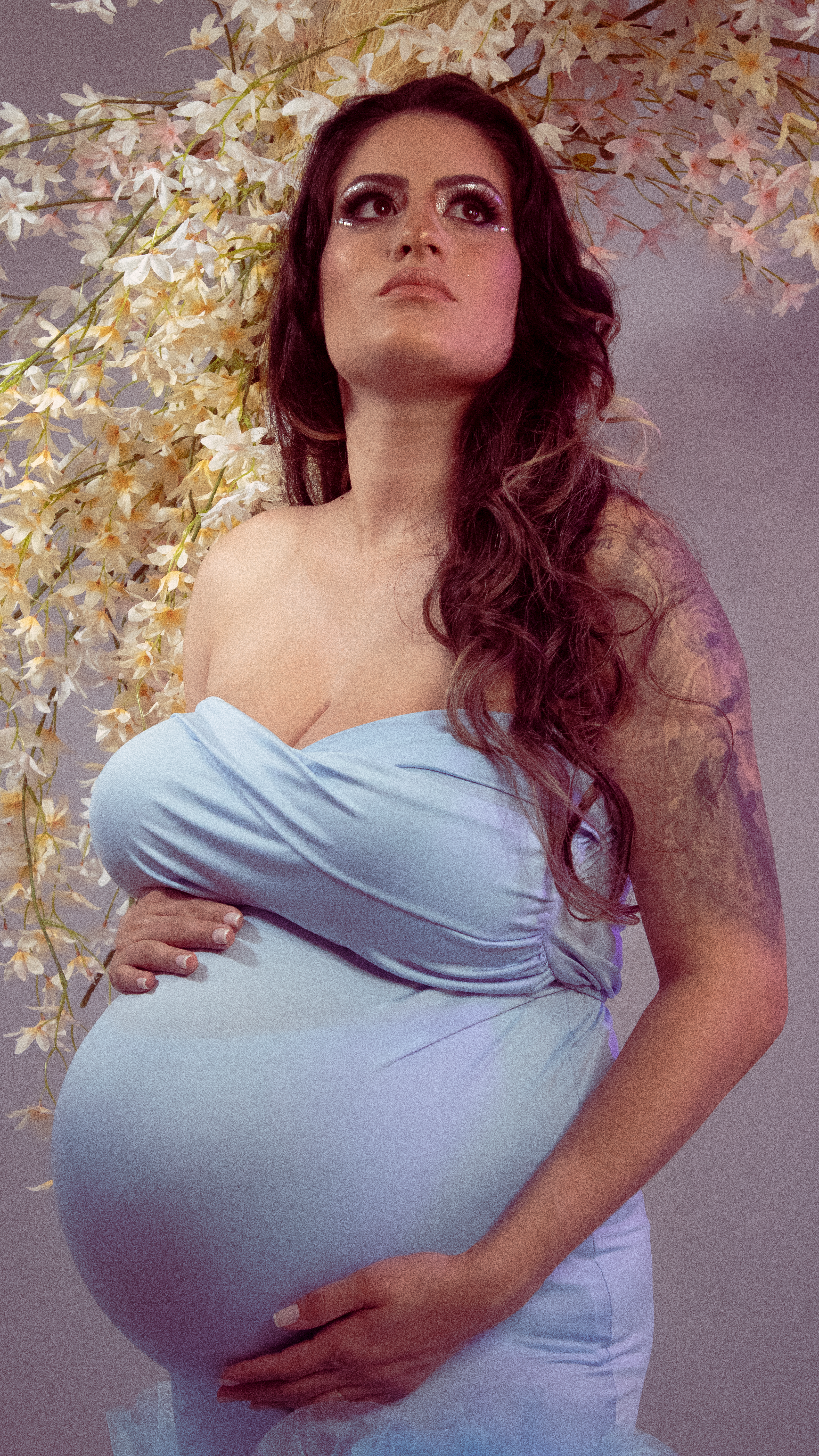 Pregnant woman in blue dress poses in a floral studio setting, capturing elegance and expectancy.