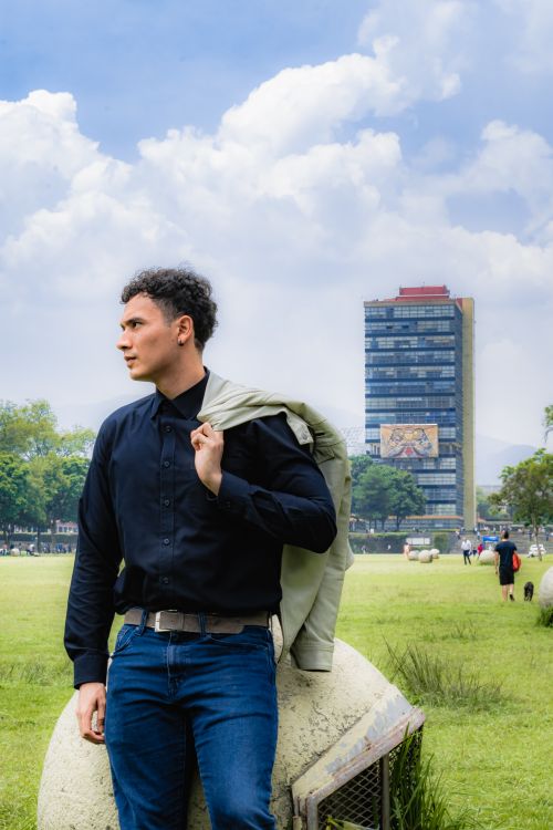 Free Man in stylish attire standing in a vibrant urban park with modern architecture in the background. Stock Photo