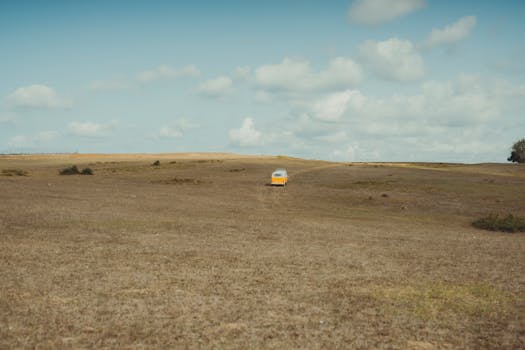 A vintage van travels across an open, rural landscape under a bright blue sky.