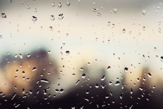 Close-up of raindrops on a window, blurring a distant cityscape, creating a moody ambiance.