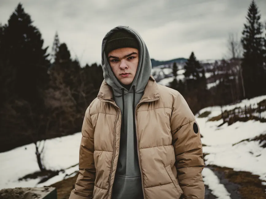 Homme en veste streetwear beige et sweat à capuche dans un décor hivernal