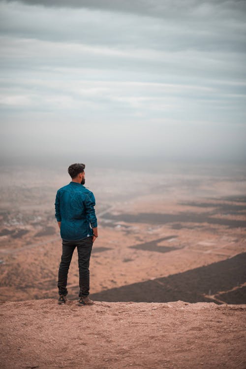 A Man in Blue Long Sleeves Standing on the Cliff